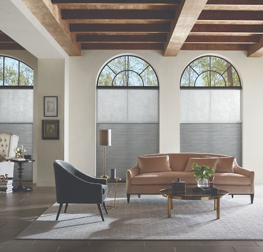 A large living room space displaying the window covering trends of Hunter Douglas Applause Honeycomb Shades over the large windows.
